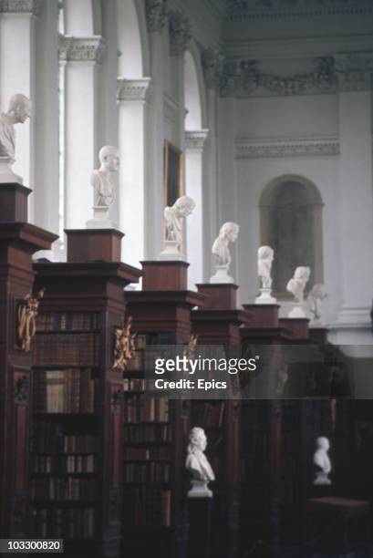 Marble busts of former members of Trinity College on display amongst bookshelves in the Wren Library, Cambridge University, circa 1975. The Wren...