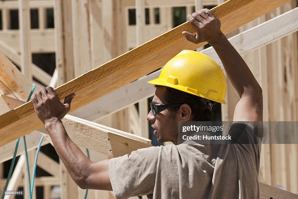 Carpenter lifting a laminated beam at a construction site