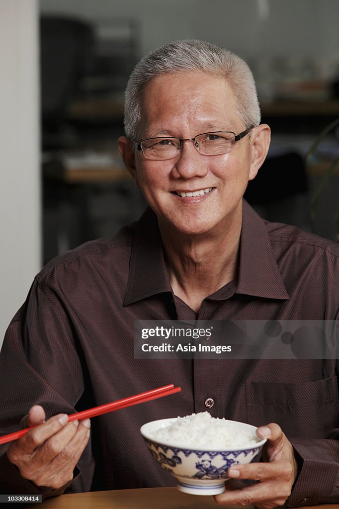 Mature man holding chopsticks and bowl of rice and smiling