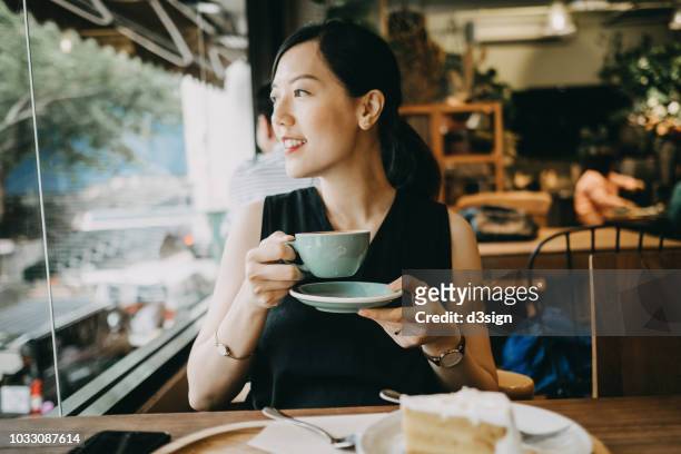 smiling woman enjoying coffee and looking through window in coffee shop - asian coffee at cafe imagens e fotografias de stock