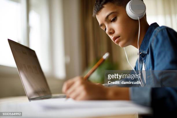 宿題をしながら音楽を聴いている十代の少年 - 少年 ストックフォトと画像