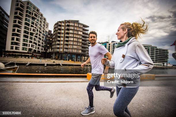 happy athlete couple jogging in city centre at sunset. - norway womens training session stock pictures, royalty-free photos & images