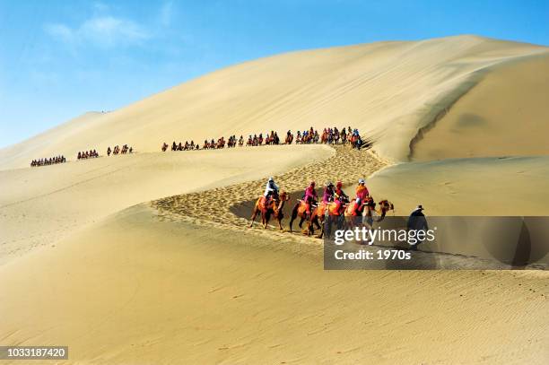 tourists were riding on the back of camels with guide in the desert of soughing dunes (mingshashan). - silk china stock pictures, royalty-free photos & images