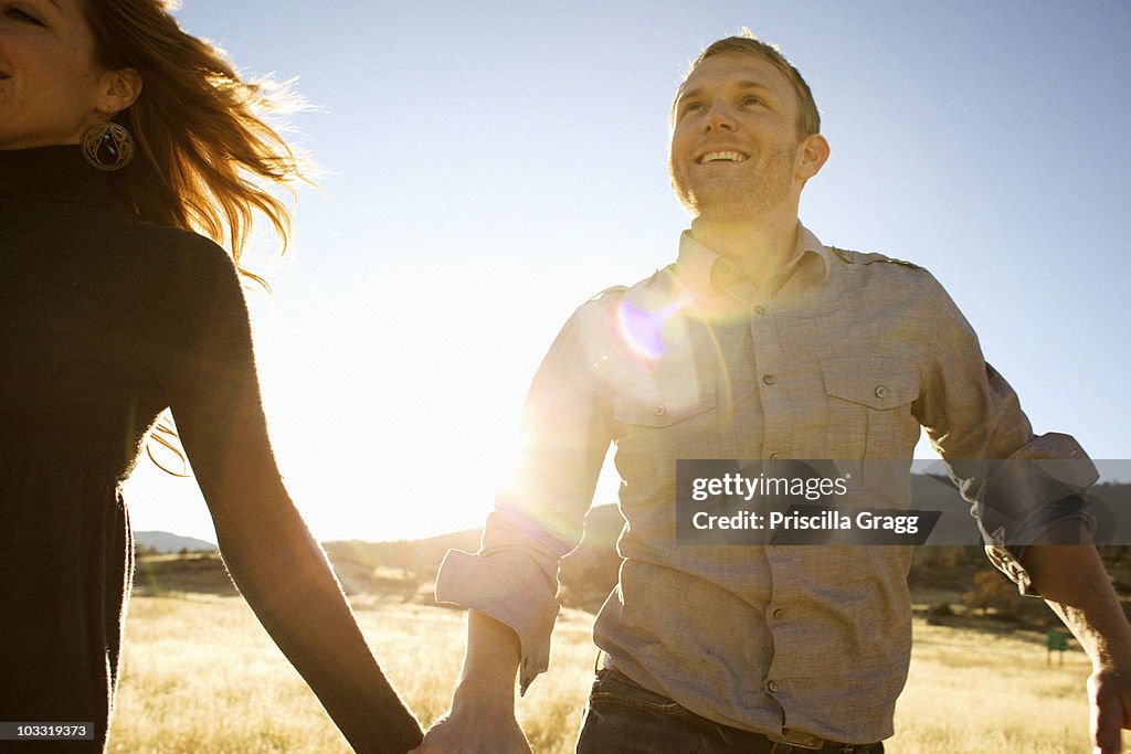 Couple run while holding hands and smiling in an open field.