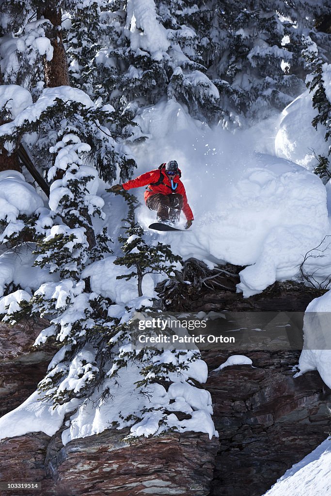 A snowboarder jumps off a cliff into powder in Colorado.