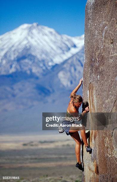 young woman bouldering in sun with snow capped mountain background. - women rock climbing stock pictures, royalty-free photos & images