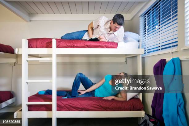 a man and woman relax on bunk beds in an adventure lodge with implied flirtatious tension. - litera fotografías e imágenes de stock