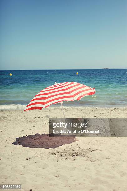 a red and white beach umbrella on the beach - parasols stockfoto's en -beelden