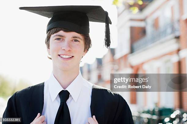 lächelnde junge tragen mütze und robe - high school graduation stock-fotos und bilder