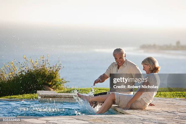 senior couple splashing feet in swimming pool overlooking ocean - senior kicking stock pictures, royalty-free photos & images