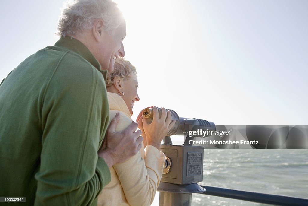 Smiling senior couple looking at ocean with coin-operated binoculars