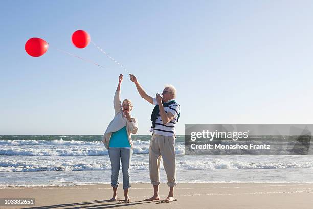 senior couple holding balloons on beach - red white and blue beach stock pictures, royalty-free photos & images