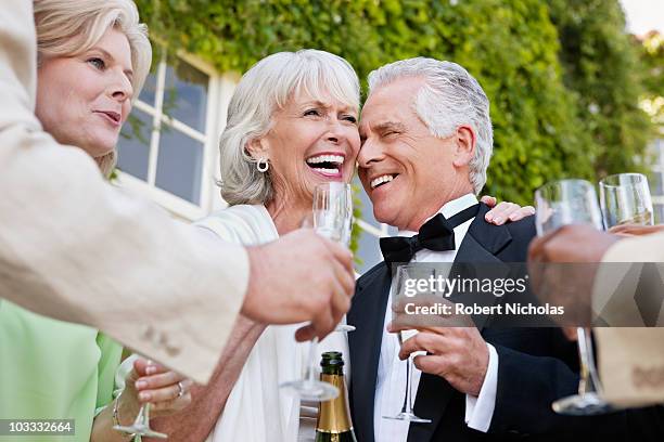 well-dressed senior couple laughing and drinking champagne - tuxedo party stock pictures, royalty-free photos & images