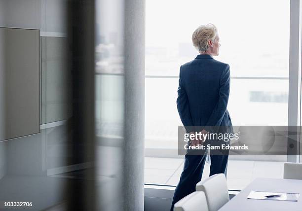 businesswoman standing at window in office - zakenvrouw stockfoto's en -beelden