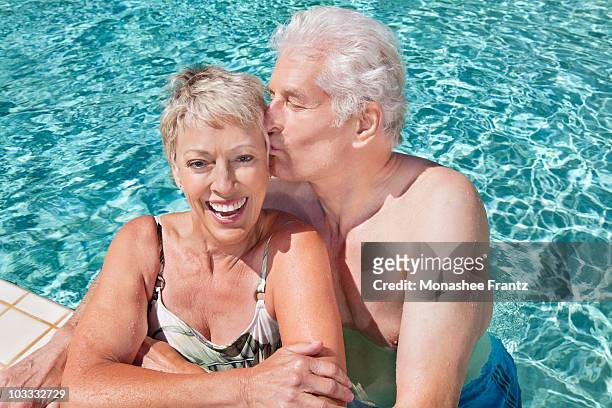 senior man kissing wife in swimming pool - chest kissing stockfoto's en -beelden