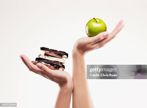 woman cupping green apple above chocolate bars - scales balance stockfoto's en -beelden