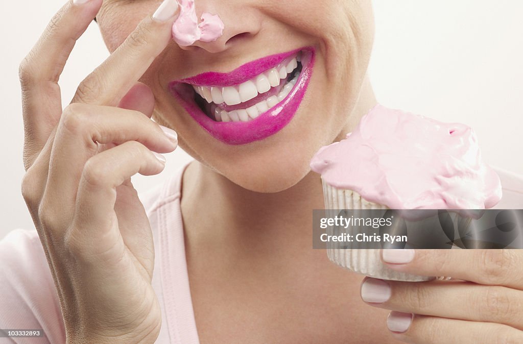 Woman with pink lipstick and frosting on nose eating cupcake