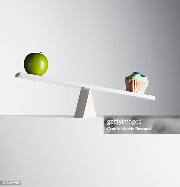 cupcake tipping seesaw with green apple on opposite end - balance cuisine stock pictures, royalty-free photos & images