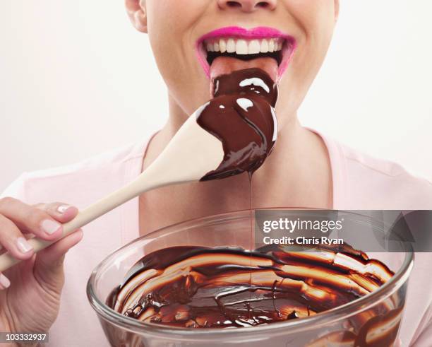 woman with pink lipstick licking chocolate batter from wooden spoon - chris chocola stockfoto's en -beelden