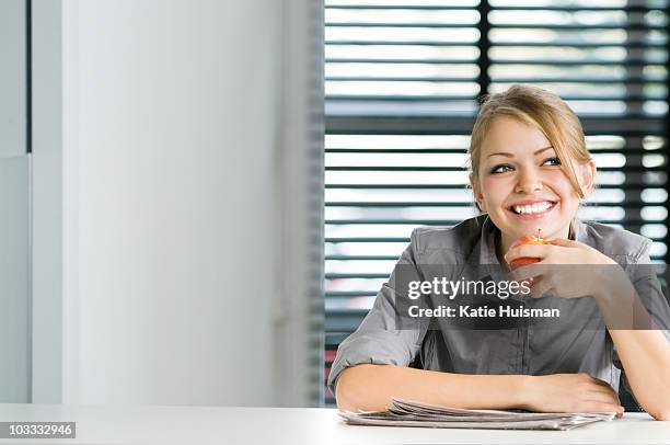 smiling businesswoman eating apple at desk - inspiring women luncheon ストックフォトと画像