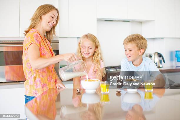 mother pouring milk for children in kitchen - milk family stockfoto's en -beelden