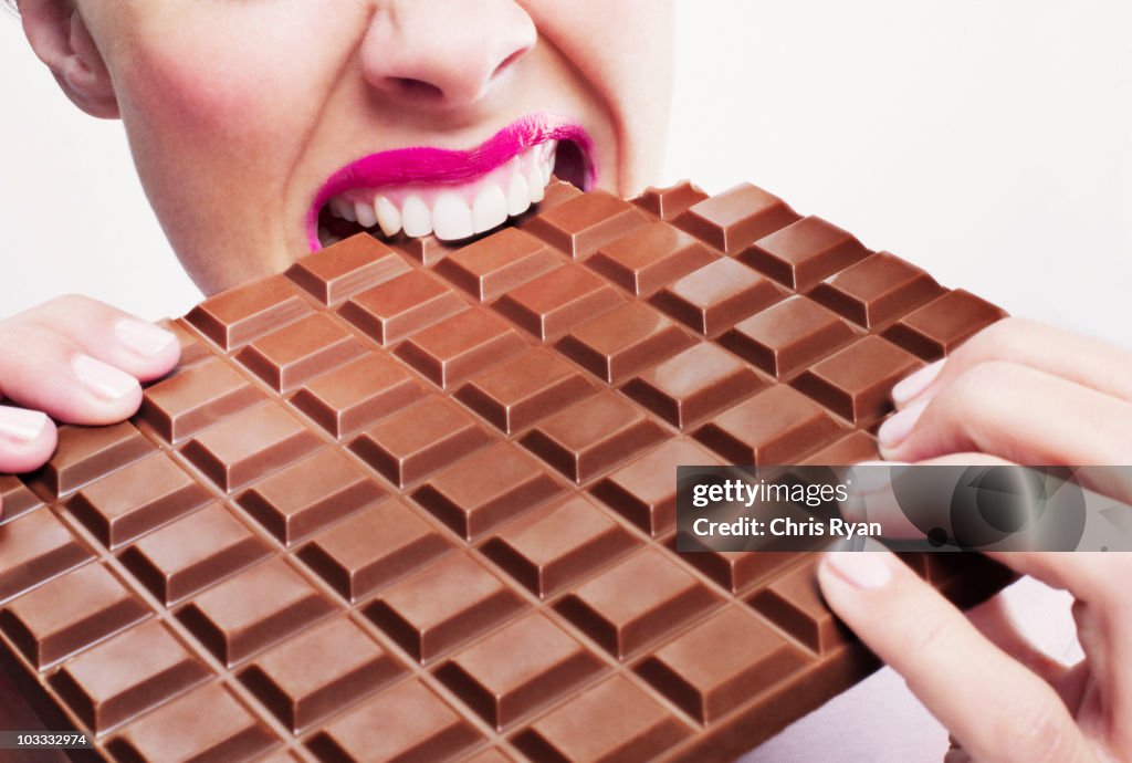 Woman in pink lipstick biting large chocolate bar