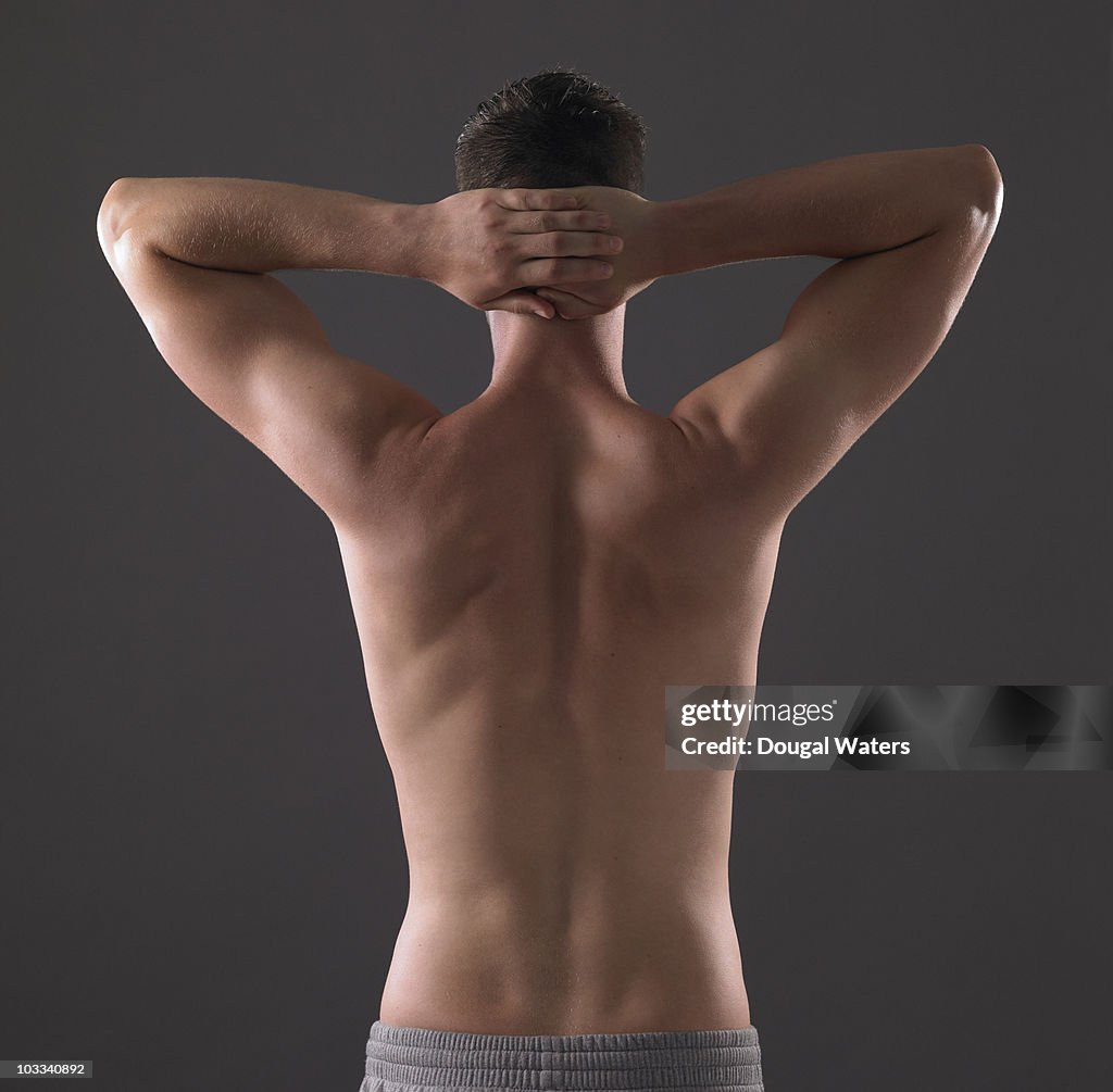 Back view of man with arms stretched behind head.