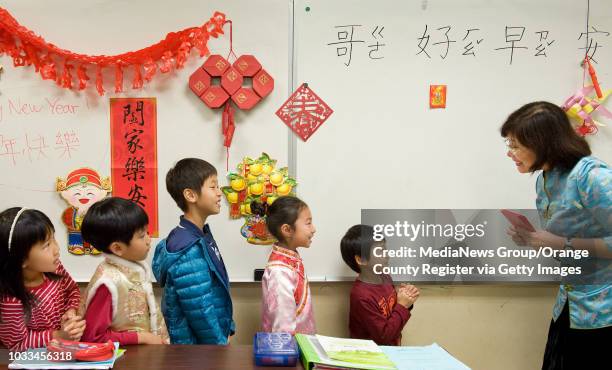 Irvine Chinese School second-grade teacher Chris Lee practices Bai Nian, or Chinese New Year greetings, with students who then get a Hong Bao, or red...