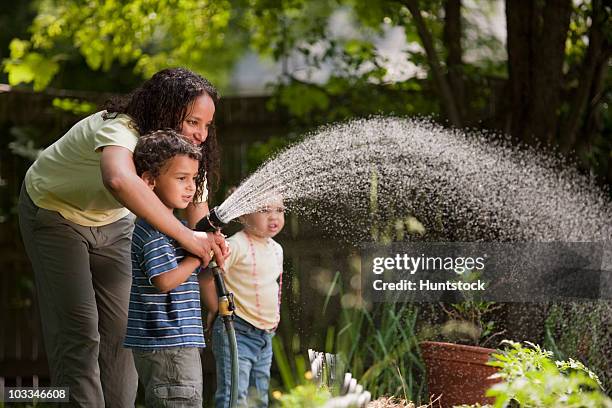 hispanic mother with her children watering in garden - two kids playing with hose stock pictures, royalty-free photos & images