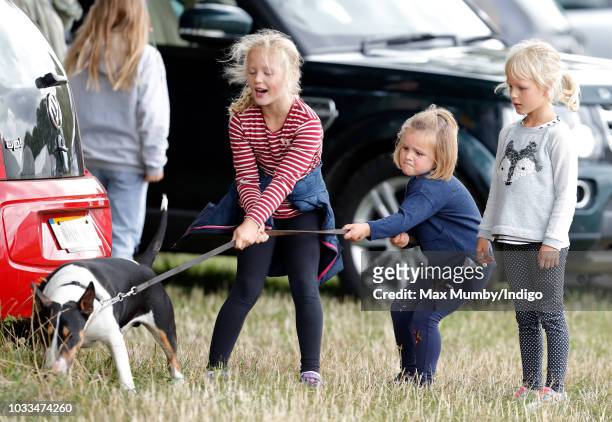 Savannah Phillips, Mia Tindall and Isla Phillips struggle to control their grandmother's bull terrier dog as they attend the Whatley Manor Horse...