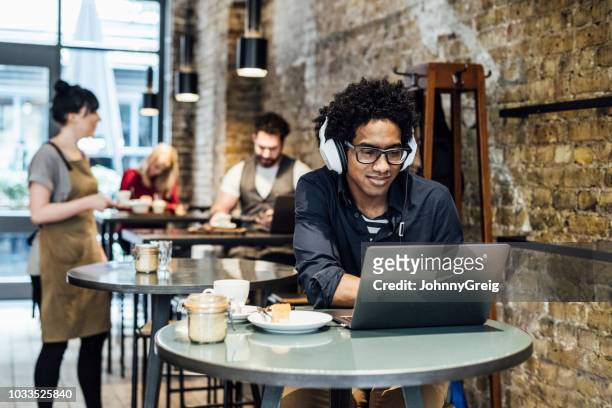 カフェでノート パソコンを使用して音楽を聴く若い男 - コーヒーショップ ストックフォトと画像