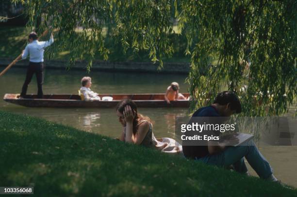 Students punting on the river Cam and catching up with some reading on the banks opposite Trinity College which is part of Cambridge University,...