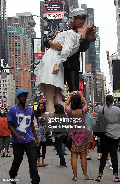 People gather beneath a 26-foot statue inspired by the iconic kiss between a nurse and a sailor in Times Square August 12, 2010 in New York City....