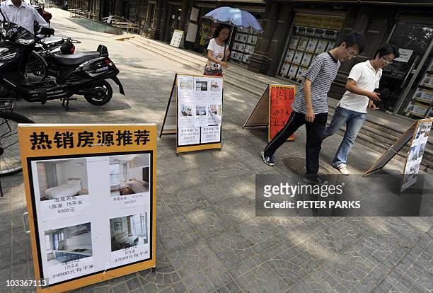 Pedestrians walk past real estate agent offices in Beijing on August 10, 2010. Property prices in China rose at a slower pace in July from the...