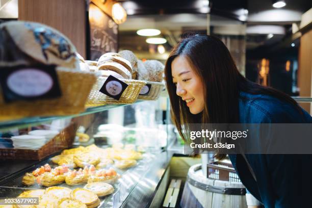 smiling young woman choosing freshly baked pastries at display window in cafe - skåp med glasdörrar bildbanksfoton och bilder