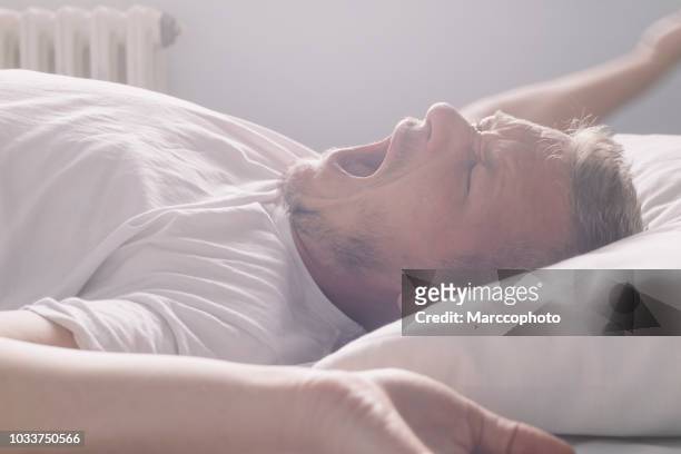 knappe volwassen man wakker in de ochtend, liggend op de rug, geeuwen en stretching - yawning stockfoto's en -beelden