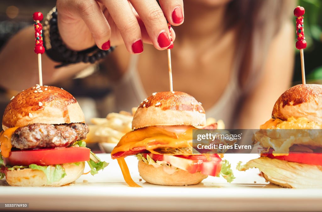 Woman eating mini burgers with fast food with French fries chips