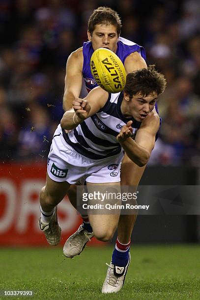 Daniel Menzel of the Cats handballs whilst being tackled by Ryan Hargave of the Bulldogs during the round 20 AFL match between the Western Bulldogs...