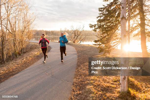 two young women running on a trail at the water's edge - anchorage foto e immagini stock