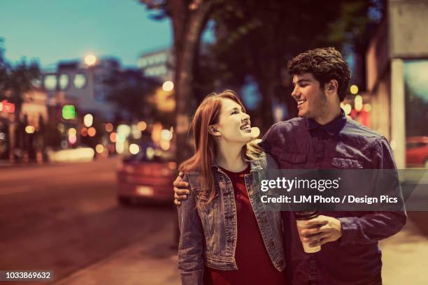 a young couple walks down a sidewalk in a popular trendy area at dusk - edmonton people stock pictures, royalty-free photos & images