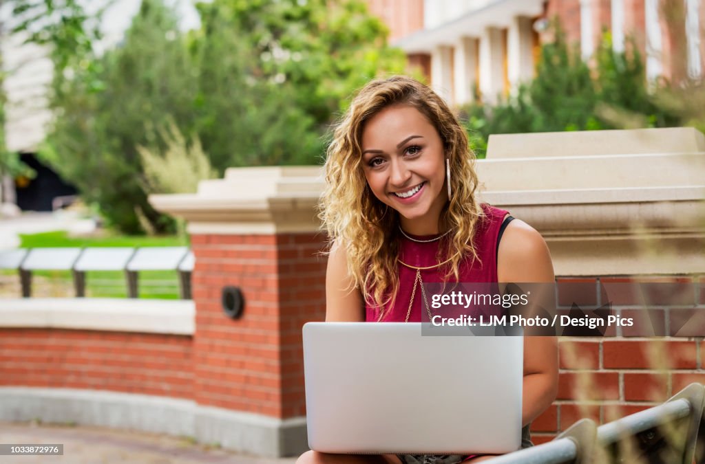 Portrait of a beautiful young female university student using her laptop outside on the campus