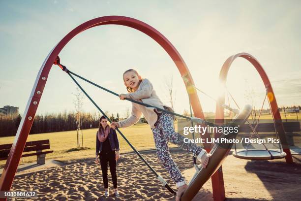 a young mom and her daughter playing on a saucer swing in a playground on a warm autumn evening - exhibition match photos et images de collection