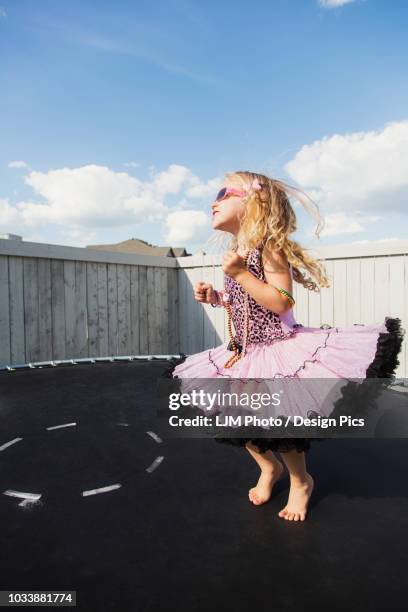 a young girl all dressed up with blond curly hair, sunglasses and jewelry standing on a trampoline in the backyard and showing off - bouncing off stock pictures, royalty-free photos & images
