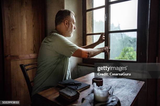 mature man closing a window on a rainy day - closing book stock pictures, royalty-free photos & images