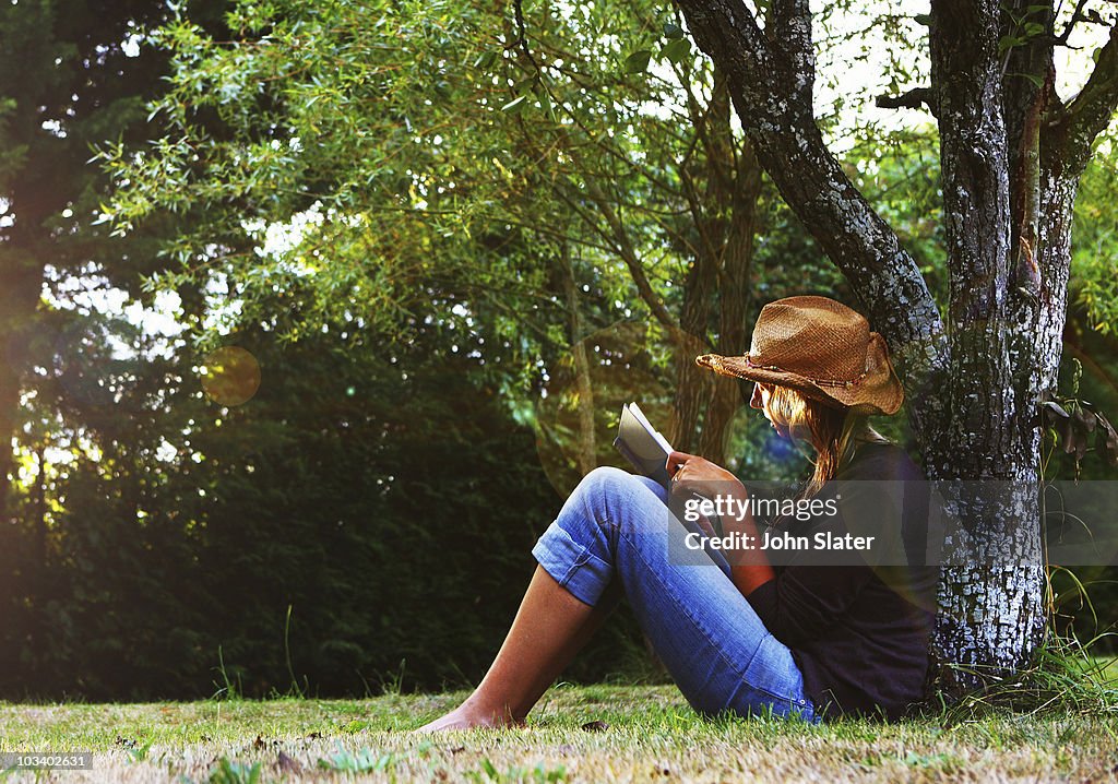 Mature woman reading book under tree