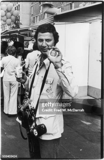 Portrait of American photogragher Ron Galella as he poses on the street and holds up a printed picture of an apple that sports a Pepsi logo; he holds...