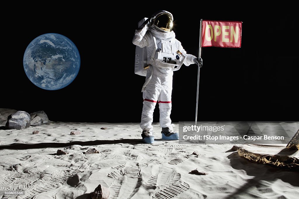 An astronaut on the moon saluting next to a flag with OPEN on it