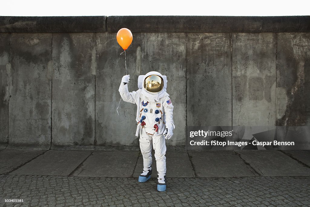An astronaut on a city sidewalk holding a balloon