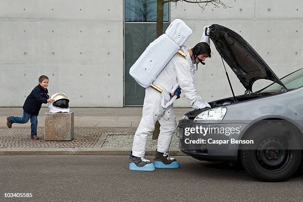 a child stealing a space helmet while an astronaut repairs his broken car - out of context stock pictures, royalty-free photos & images