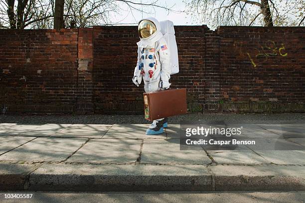 an astronaut carrying a suitcase and walking on a city sidewalk - leaving stock-fotos und bilder